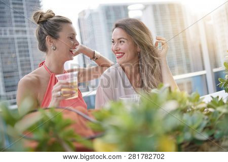 Two attractive funloving friends partying with drinks on rooftop bar in city