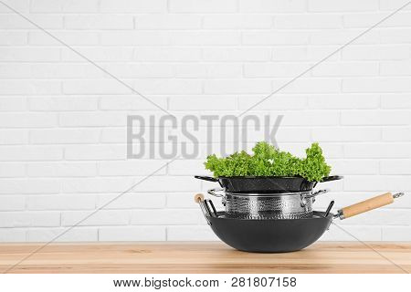 Stack Of Clean Cookware With Lettuce On Table Against White Brick Wall. Space For Text