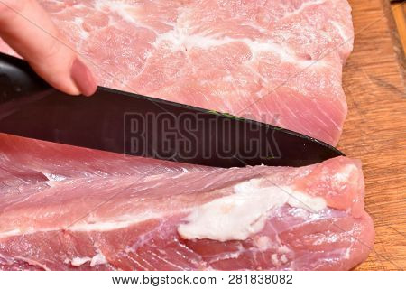 Cutting Pork Meat With A Black Knife, Close-up, On A Cutting Board. Pork Meat Ribs
