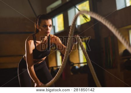 Fit, sporty and athletic sportswoman working in a gym. Woman training using battle ropes. Sports, athletics and fitness concept.