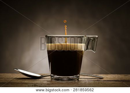 Black Coffee In Glass Cup With Teaspoon And Jumping Drop, On Wooden Table