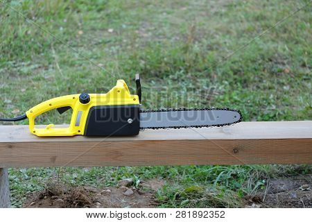New Black And Yellow Electric Saw On Brown Wooden Balk Ready For Work Outdoors Closeup View