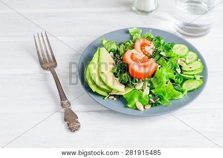 Fresh  Green Salad With Cucumber, Lettuce, Avocado And Tomatoes And Glass Water On A White Wooden Ta