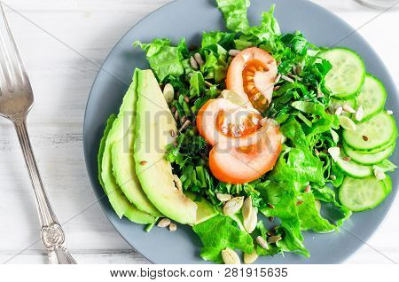 Fresh  Green Salad With Cucumber, Lettuce, Avocado And Tomatoes And Glass Water On A White Wooden Ta
