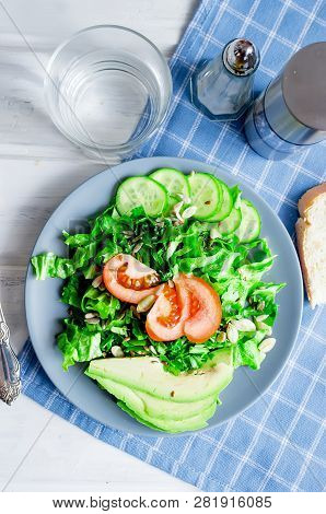 Fresh  Green Salad With Cucumber, Lettuce, Avocado And Tomatoes And Glass Water On A White Wooden Ta
