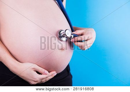 Pregnant Woman Holding Phonendoscope On Her Belly On Blue Background. Medical Examination During Pre