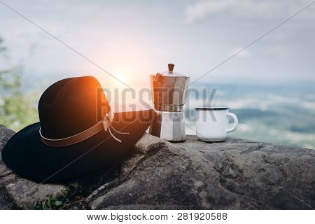 Cup Hot Coffee, Hat And Coffee Maker On Background Of Nature During The Sunset . Concept Adventure A