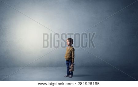 Little waggish kid staying alone in a big empty room with his plush