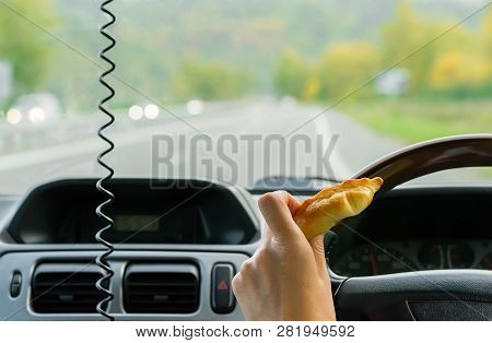 Closeup, Of Female Hand Holding A Bun Behind The Wheel Of The Car In Motion On Highway