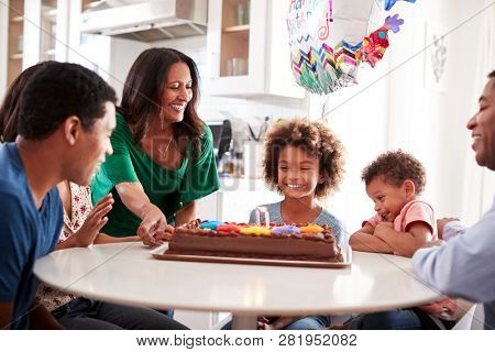Close up of three generation family sitting together at the kitchen table celebrating the pre-teen daughters birthday with a birthday cake