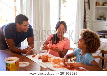 Millennial dad leaning on table watching his daughter and her girlfriend playing with modelling clay in the dining room