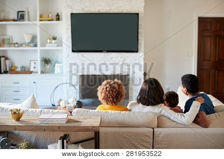 Back view of young family sitting on the sofa and watching TV together in their living room