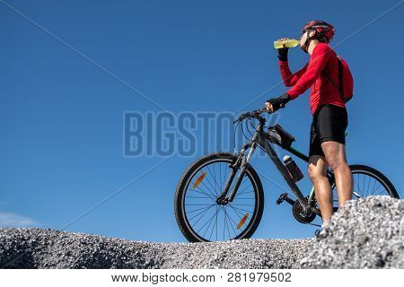 Cyclist Resting And Drinking Isotonic Drink. Backlight, Sunny Summer Day. Extreme Mountain Bike Spor