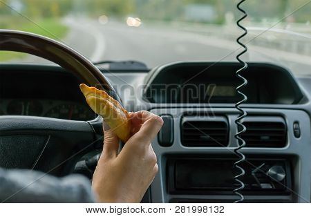 Closeup, Of Female Hand Holding A Bun Behind The Wheel Of The Car In Motion On Highway