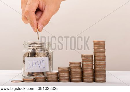 Hand Of Male Putting Coins In Jar With Money Stack Step Growing Growth Saving Money With Gray Backgr