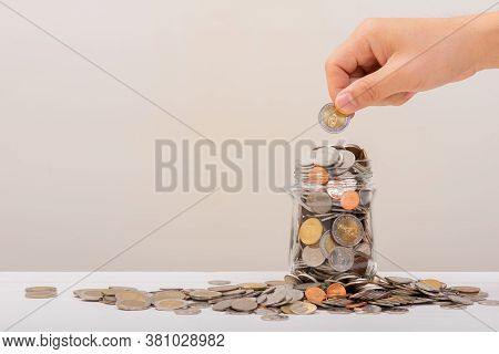 White Hand Man Holding Gold Coin To Putting In Jar Or Glass Bottle For Saving With Soft White Backgr