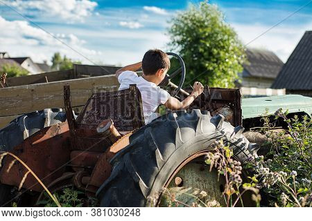 A 10-year-old School-age Boy Tries To Start An Old Tractor Or Car. Repair. Little Helper. Harvest Ti