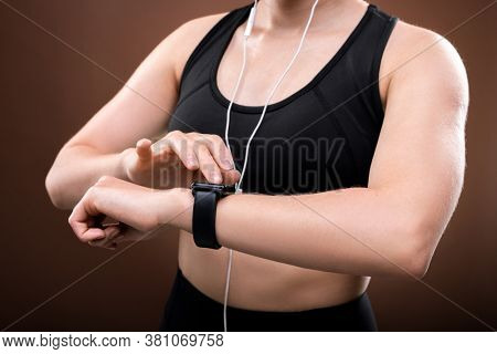Mid section of young sportswoman in activewear and earphones switching on her fitbit on wrist before outdoor jogging workout