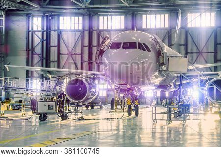 Civil Airplane Jet On Maintenance Of Engine And Fuselage Check Repair In Airport Hangar. Bright Ligh