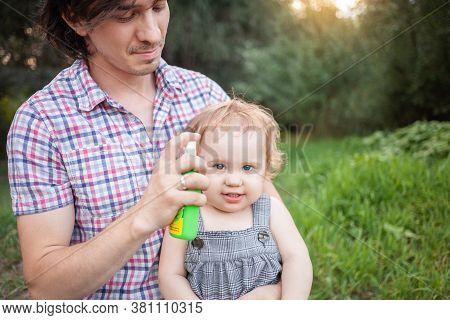 Dad Treats His Daughter With Mosquito Spray. The Man Uses Spray On The Childs Arms And Legs. Protect