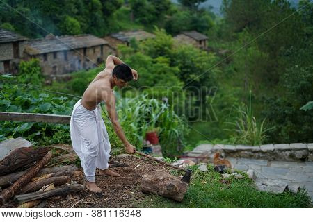 A Young Boy Wearing A White Dhoti Chopping Wood With An Axe.