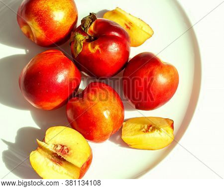 Red Ripe Organic Nectarine Fruits On The White Plate On Nature Background. Summertime Healthy Eating