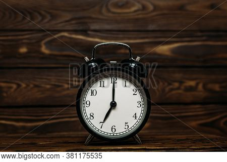 Clock On A Wooden Background. The Clock Shows The Time Of Seven O'clock In The Afternoon. The Clock 