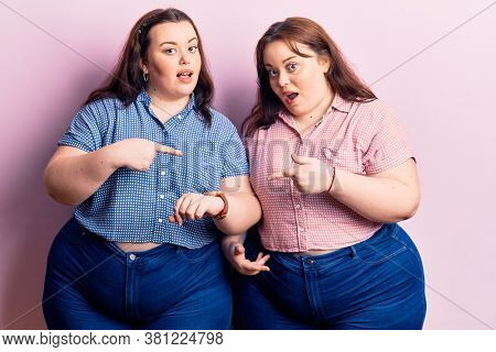 Young plus size twins wearing casual clothes in hurry pointing to watch time, impatience, upset and angry for deadline delay 