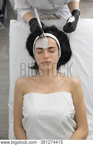 Beautiful Young Woman At The Reception Of A Beautician, Skin Enzymatic Peeling. Apply A White Mask T