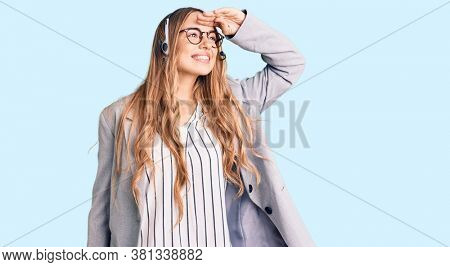 Young beautiful blonde woman wearing call center agent headset very happy and smiling looking far away with hand over head. searching concept. 