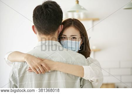 Young Asian Woman Wearing Mask Hugging Husband Looking At Camera