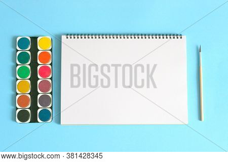 Art Concept. Back To School. Watercolors With White Notebook And Brush On Blue Background.