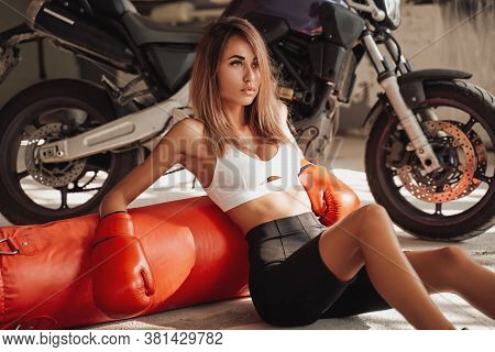 Pretty And Attractive Sportswoman Posing In A Light Studio Sitting On The Floor With A Large Orange 