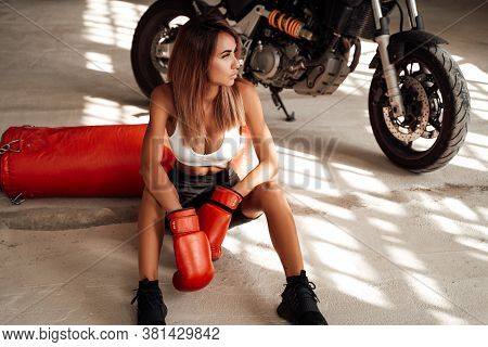 Pretty And Skinny Sportswoman Posing In A Light Studio Sitting On The Floor With A Large Orange Punc