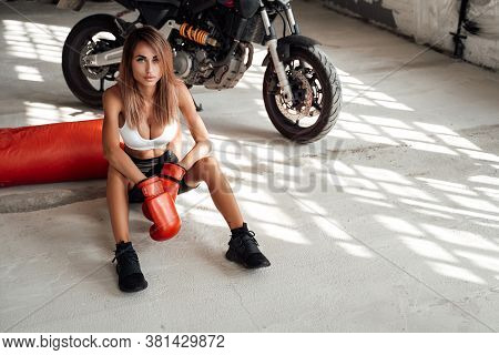 Sexy And Attractive Looking Young Sportswoman Posing In A Light Studio Sitting On The Floor With A L
