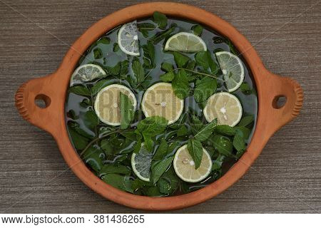 Sliced Lemon With Mint Sprigs In Water In A Clay Container. High Quality Photo