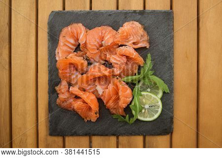 Slices Of Lightly Salted Salmon On A Black Plate Close Up On A Wooden Table.