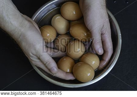 Male Hands Take Chicken Eggs From A Metal Bowl Of Water. A Portion Of Boiled Eggs Is Cooled In A Met