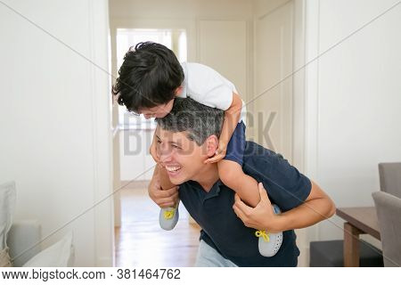 Joyful Little Boy Sitting On Father Shoulders And Laughing. Happy Handsome Caucasian Dad In Shirt Ho
