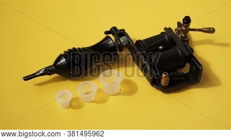 Tattoo Equipment, Tattoo Ink Plastic Caps And Tattoo Machine On Yellow Background
