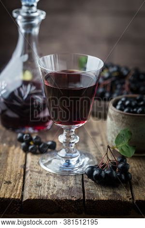 Homemade Black Chokeberry Wine Or Liqueur With Ripe Berries On Wooden Background