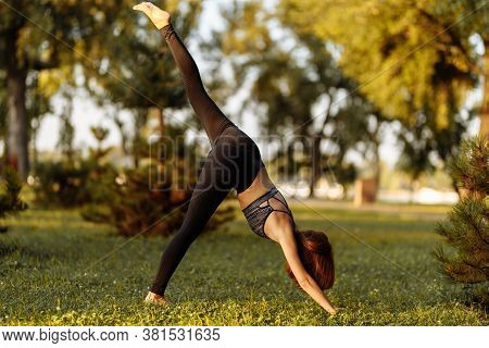 Fitness And Yoga In Nature. The Girl Is Warming Up And Medinating In The Park.