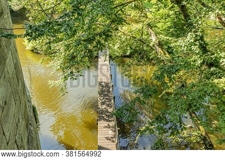 Top Perspective Of Abundant Green Foliage And A Wooden Footbridge Over The Jeker River In Maastricht
