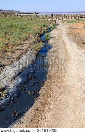 Spilled Streams Of Liquid Crude Oil Flow Down Drainage Ditch Into Public Body Of Water. Environmenta