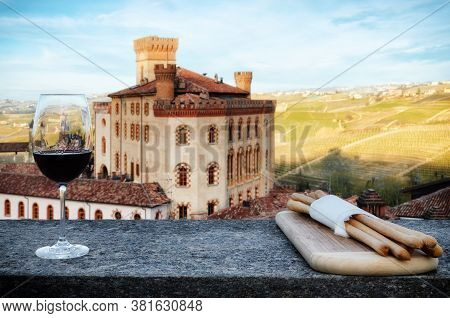 A Chalice Of Barolo Red Wine On A Windowsill With Breadsticks And The Castle Of Barolo (piedmont, It
