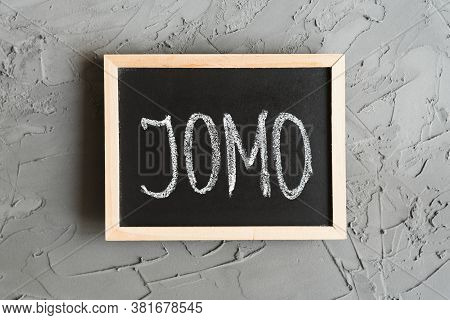 Jomo Concept. Jomo Means Joy Of Missing Out. Acronym Written On A Small Blackboard, Concrete Wall As