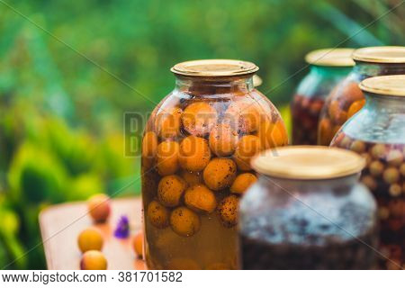 Jars With Kompot On Table. Sealed Glass Jars With Kompot Placed On Table Near Flowers And Fruits On 