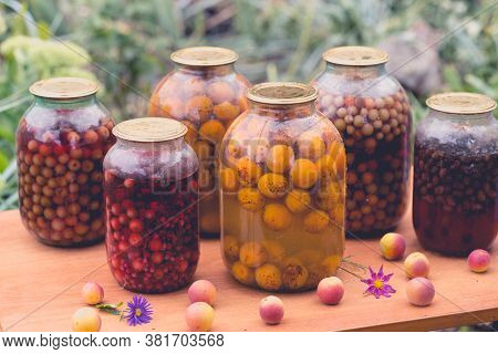 Jars With Kompot On Table. Sealed Glass Jars With Kompot Placed On Table Near Flowers And Fruits On 