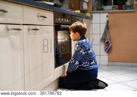 Cute Funny Blond Kid Boy Baking Muffins In Domestic Kitchen. Child Having Fun With Helping, Sitting 