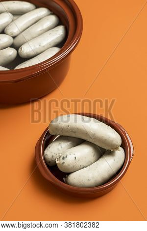Eating White Sausage In A Ceramic Plate, On An Orange Seamless Background. German Veal Sausage Boile